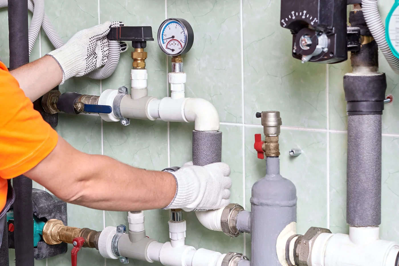 Technician adjusting hydronic heating pipes and a pressure gauge in a mechanical room