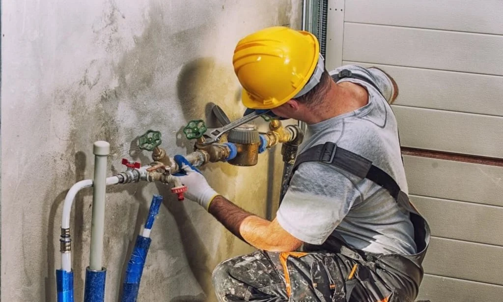 Plumber in a hard hat repairing the main water shut-off valve and meter connection