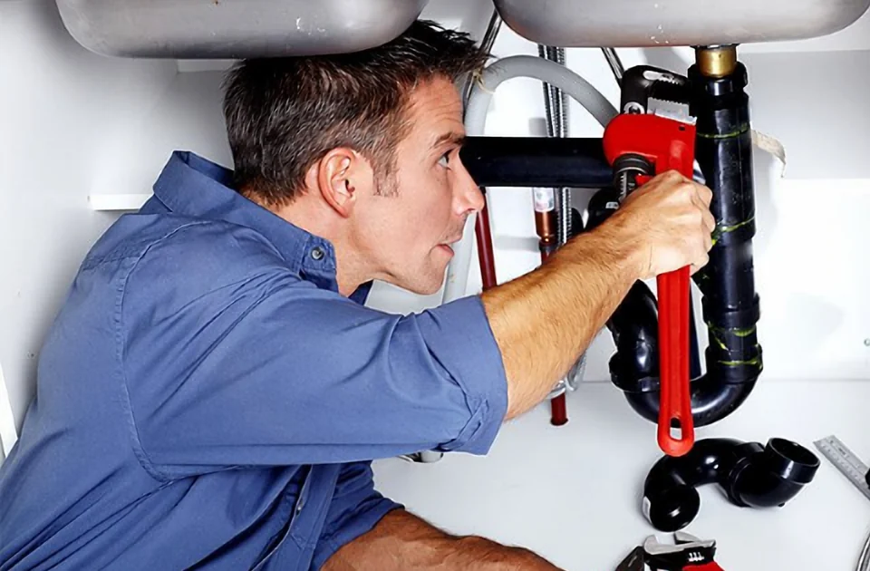Plumber tightening a sink drain pipe with a red pipe wrench during a plumbing repair in Toronto
